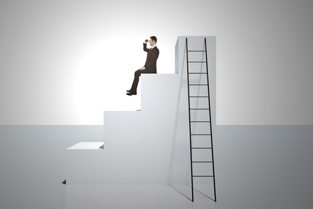 Businessman looking into the distance on top of stairs with ladder on white background. Research and growth concept.の写真素材