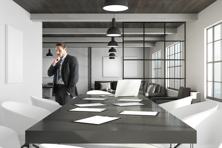 Pensive young european businessman standing in modern office interior. Boss and research concept.の写真素材