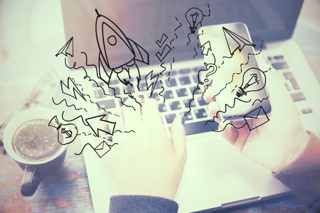 Close up of hands using smartphone and laptop keyboard with startup sketch and coffee cup on desk. Entrepreneurship and launch conceptの写真素材