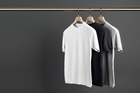 Empty grey, white and black shirts on hanger. Concrete wall background. Design, store and style concept. Mock up, 3D Renderingの写真素材