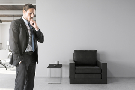 Thoughtful young european businessman standing in modern office interior with copyspace. Boss and research concept.の写真素材