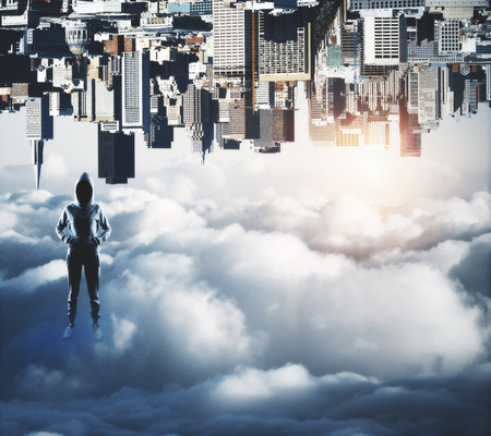 Confident hakcer standing on abstract upside down city background with clouds and copy space. Malware and phishing conceptの写真素材