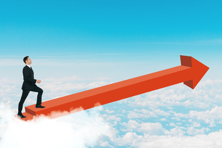 Side view of young businessman walking on red arrow on sky background. Success and growth conceptの写真素材