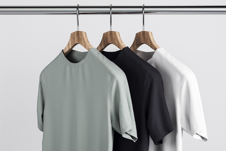 Empty grey, white and black t-shirts on hanger. Concrete wall background. Design, store and style concept. Mock up, 3D Renderingの写真素材