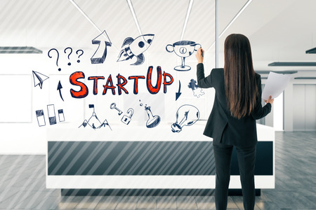 Back view of attractive young european businesswoman drawing start up sketch in modern office reception interior. Startup and seminar concept.の写真素材