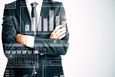 Unrecognizable businessman with folded arms standing on white background with business charts. Finance and analytics concept. Double exposureの写真素材