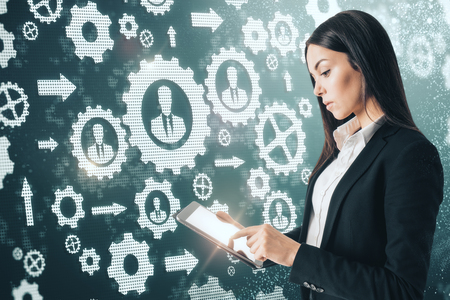 Side view of attractive young european businesswoman using tablet on abstract cogwheels background.の写真素材