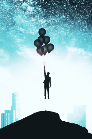 Backlit person with balloons on hill standing on beautiful starry night sky city background. Freedom and opportunity conceptの写真素材