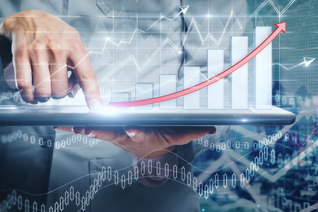 Close up of hand using tablet with business chart hologram on blurry office interior background. Report and invest concept. Double exposureの写真素材