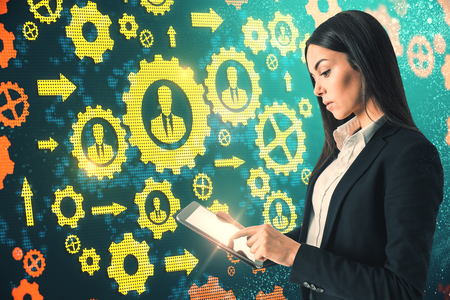 Side view of pretty young european businesswoman using tablet on abstract cogwheels background.の写真素材
