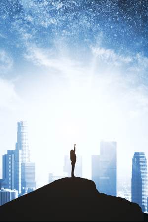 Confident backlit superhero on hill and starry sky and city background. Purpose and confidence conceptの写真素材