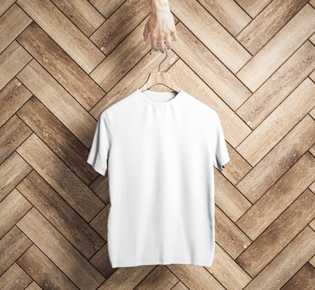 Hand holding hanger with empty white t-shirt on wooden plank wall background. Design and shop concept. Mock up, 3D Renderingの写真素材