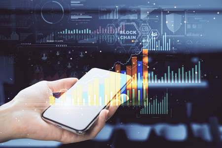 Close up of hand using device with glowing business chart hologram on blurry background. Technology and economy concept. Double exposureの写真素材