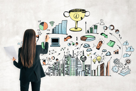Economy and success concept. Back view of young businesswoman drawing business sketch on concrete wallの写真素材