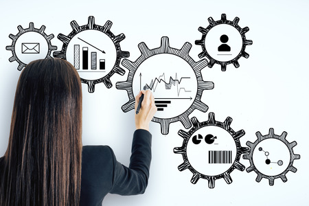 Businesswoman drawing creative cogwheels sketch on concrete wall background. Engineering and success conceptの写真素材
