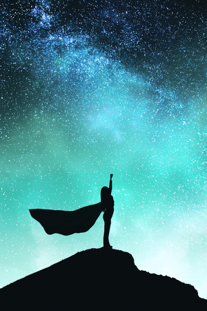 Confident backlit superhero with cape silhouette standing on mountain and starry sky background. Success and confidence concept