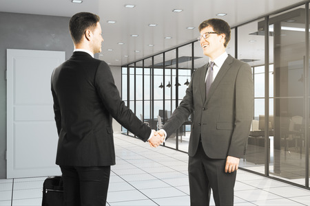 Happy european businessmen shaking hands in modern office interior. Teamwork and success concept.の写真素材