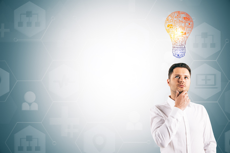 Attractive thoughtful young european businessman with lamp standing on light background with copy space. Technology and inspire conceptの写真素材