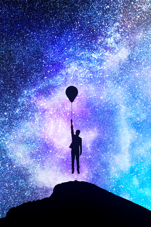 Backlit person with balloons on hill standing on beautiful starry night sky space background. Freedom and inspire conceptの写真素材