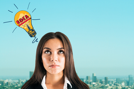 Portrait of attractive young european businesswoman with lamp sketch on blurry city and sky background. Idea and achievement conceptの写真素材
