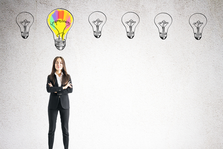 Portrait of attractive happy young european businesswoman with folded arms and drawn lamps standing on concrete wall background. Idea and purpose conceptの写真素材