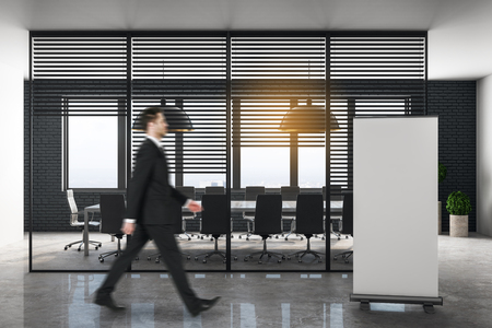 Side view of young businessman walking in modern office meeting room interior with empty poster. Corporate and professional concept. Mock up,の写真素材