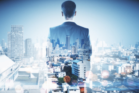 Back view of businessman on blurry bokeh city background. Success and ambition concept. Double exposureの写真素材