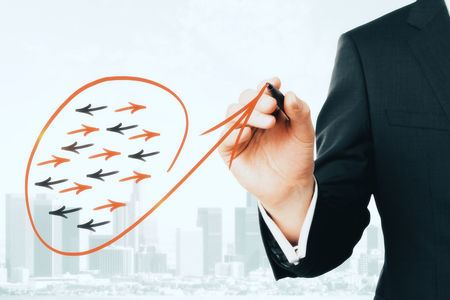 Businessman hand drawing creative arrow sketch on light blurry city background. Different direction and leadership conceptの写真素材