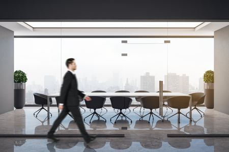 Side view of attractive young european businessman walking in conference meeting room with city view. Executive and boss concept.の写真素材