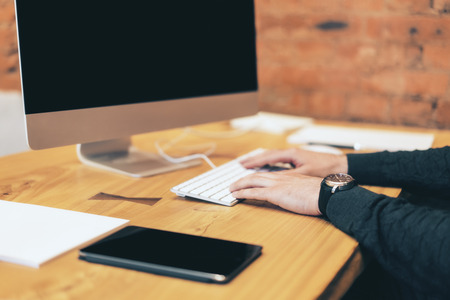 Side view of businessman hands using computer on wooden desktop and blurry red brick wall background. Worker, technology and education conceptの写真素材