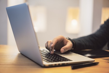 Side view of man hands using notebook keyboard on wooden desktop workplace. Blurry background....