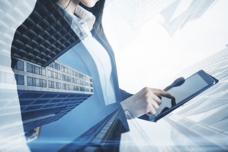 Side view of unrecognizable businesswoman using tablet on blurry city background. Technology and communication concept. Double exposureの写真素材
