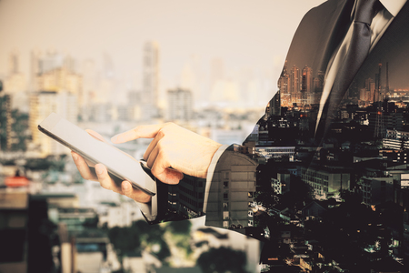 Side view of unrecognizable businessman using tablet on blurry city background. Technology and network concept. Double exposureの写真素材