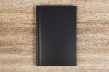 Blank closed black hardcover book on wooden desktop background. Close up. Publish and info concept. Mock up, 3D Renderingの写真素材