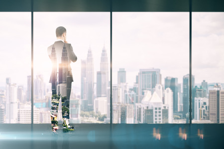 Back view of thoughtful young businessman standing in modern business interior with Kuala Lumpur city view. Trade and research concept. Multiexposureの写真素材