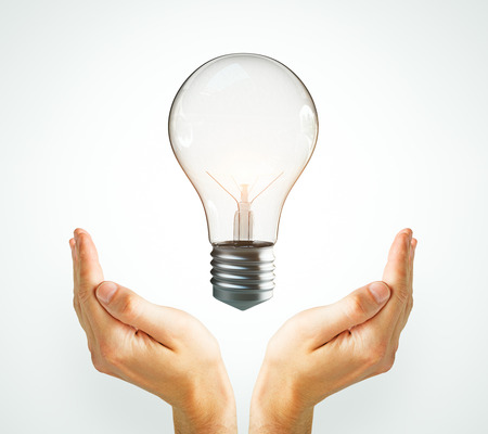 Idea and success concept. Two hands holding light bulb on subtle backgroundの写真素材
