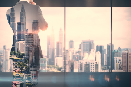 Back view of thoughtful young businessman standing in modern business interior with Kuala Lumpur city view. Success and research concept. Double exposure