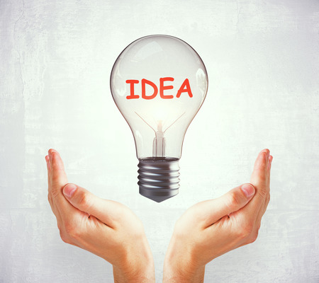 Idea and solution concept. Two hands holding light bulb on subtle backgroundの写真素材