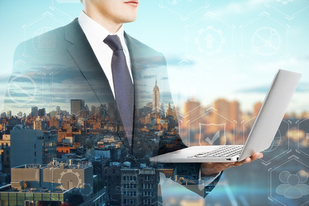 Side view of attractive young european businessman using laptop on blurry city background. Network and success concept. Double exposureの写真素材