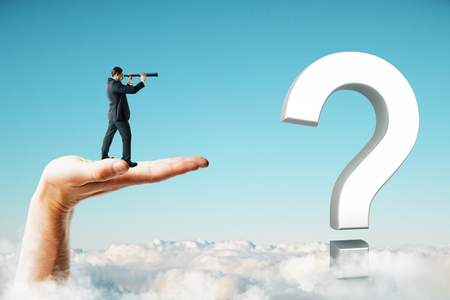 Businessman with telescope standing on abstract hand and white question mark and looking into the distance. Blue sky background. Direction, vision, doubt and success conceptの写真素材