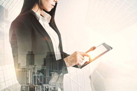 Young european businesswoman using tablet on abstract city background. Technology and communication concept. Multiexposureの写真素材