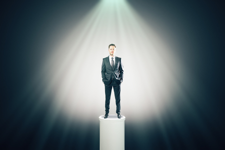 Attractive businessman standing on illuminated pedestal. Success and leadership conceptの写真素材