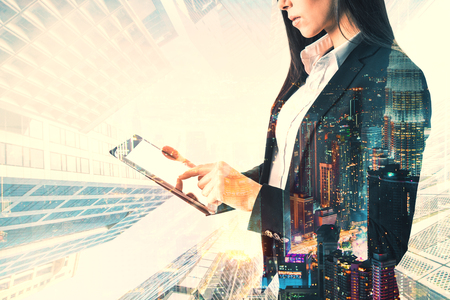Side view of young european businesswoman using tablet on blurry city background. Technology and communication concept. Double exposureの写真素材