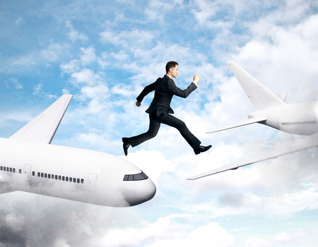 Businessman jumping from plane to plane on blue sky background with clouds. Freedom and challenge conceptの写真素材