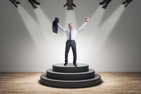 Best employee and leadership concept. Happy businessman standing on illuminated pedestal on concrete backgroundの写真素材
