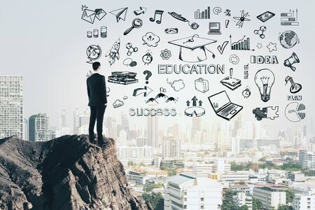 Knowledge and idea concept. Businessman standing on cliff with creative education sketch on modern city background. Double exposureの写真素材