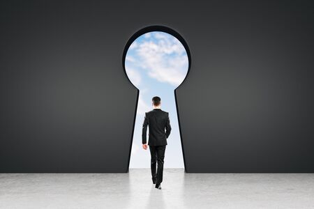 Back view of young businessman in abstract black interior with keyhole window and sky view. Access and leadership conceptの写真素材