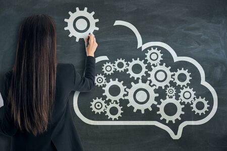 Data storage network technology concept. Businesswoman with creative cloud and cogs sketch on chalkboard backgroundの写真素材
