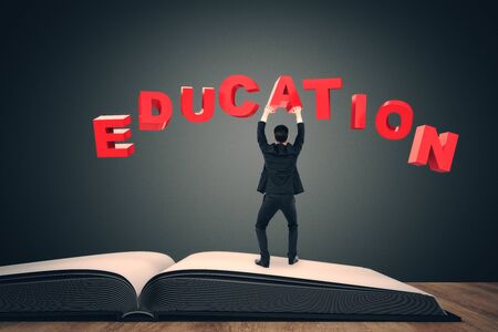 Back view of young businessman standing on open book page while holding education word. Success and knowledge condept.の写真素材