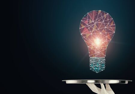 Hand holding silver tray with creative polygonal light bulb on dark background. Innovation, technology and solution conceptの写真素材